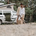 A couple shares a romantic moment by their camper van in a serene outdoor setting.