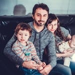 A joyful family of four sitting on a sofa, smiling warmly indoors.