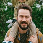 Happy father carrying son on shoulders in a blooming garden setting.