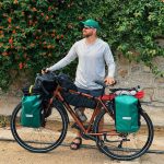 Male cyclist with touring gear against lush flowering backdrop.