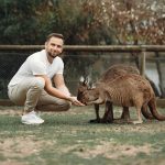 Side view full body content stylish man bending to hand feed cute kangaroos while spending time in kangaroo sanctuary in daytime