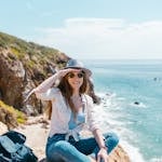 Young woman sitting on cliffs by the ocean, enjoying a sunny day outdoors.
